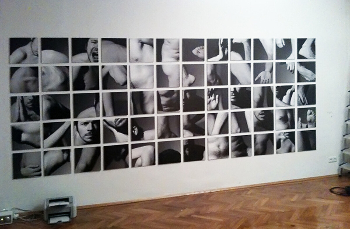 The sixty prints pinned edge to edge in five rows of twelve on a white wall above a parquet floor