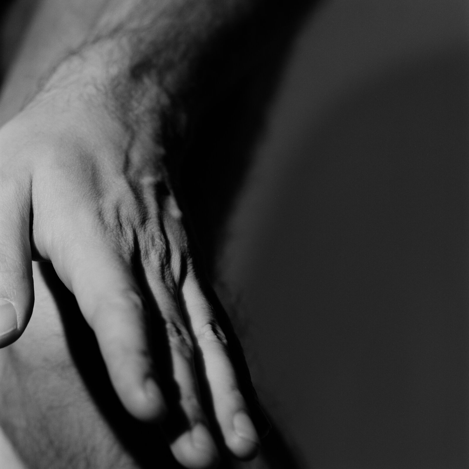 A hand resting against a knee, the fingers spread, in raking light