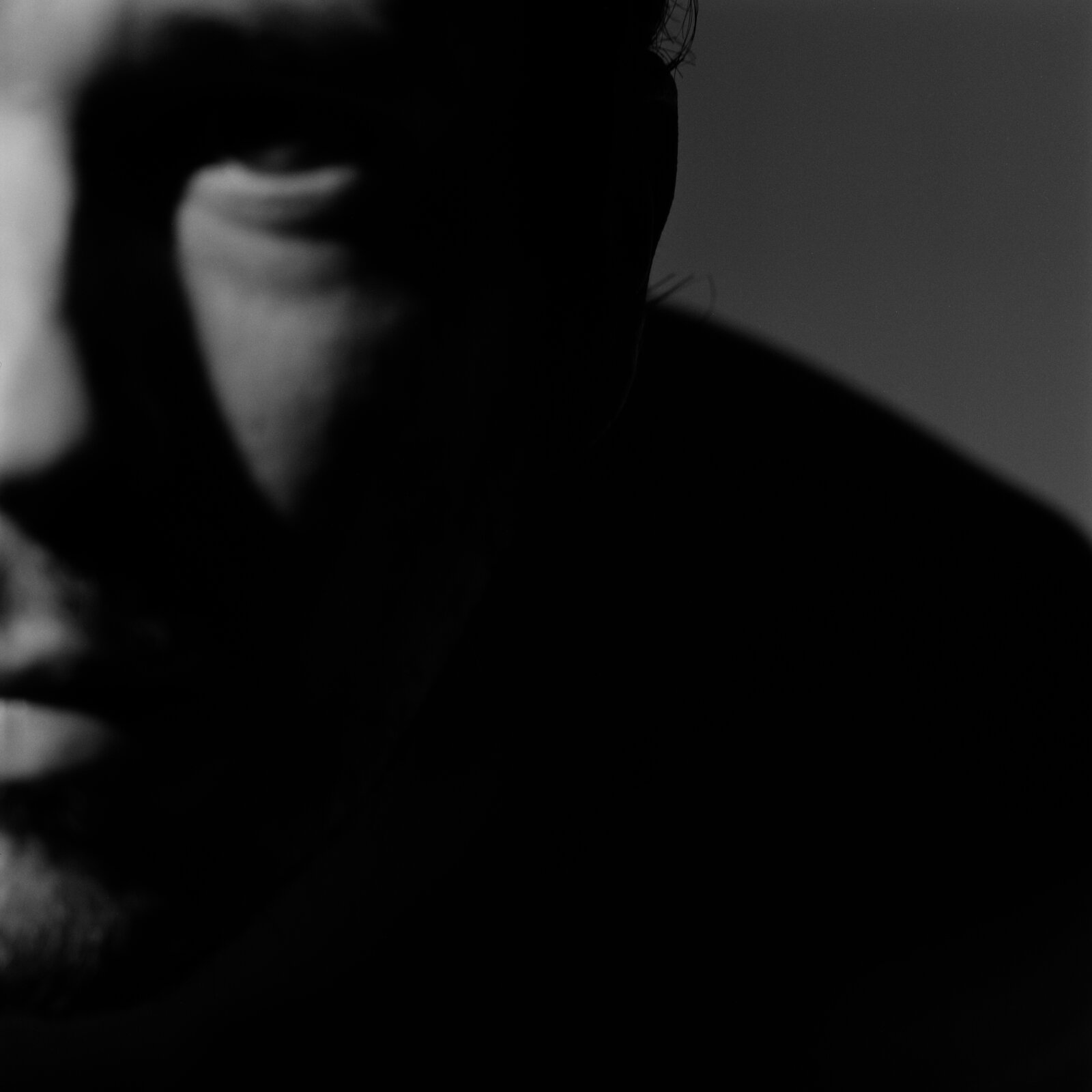 A face in deep shadow, only the mouth and the line of the jaw in light