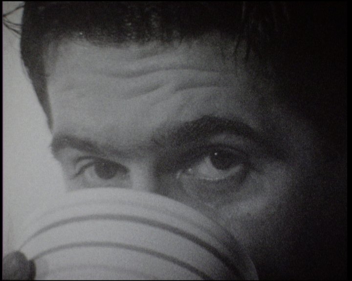 A man drinking from a striped bowl, eyes lifted over its rim towards the camera