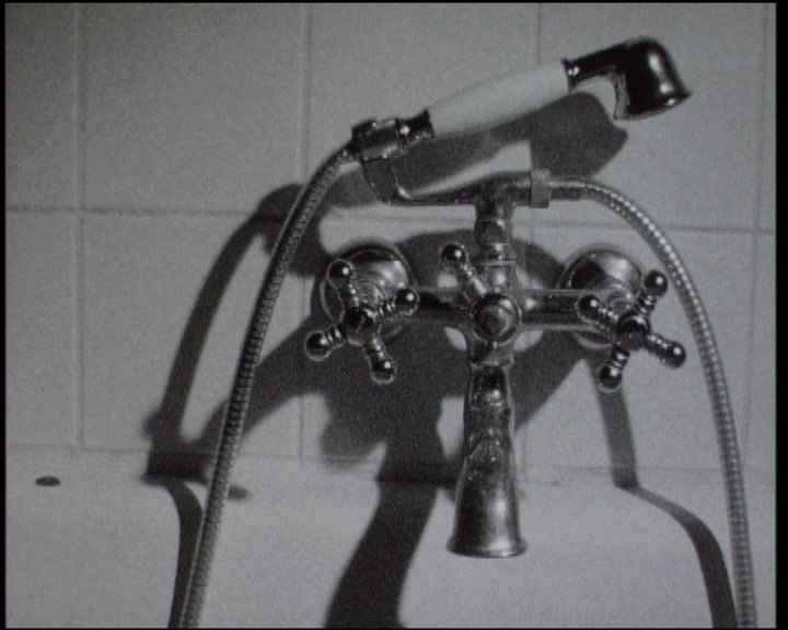 A chrome bath tap and shower hose against white tiles, the shower head resting on the mixer