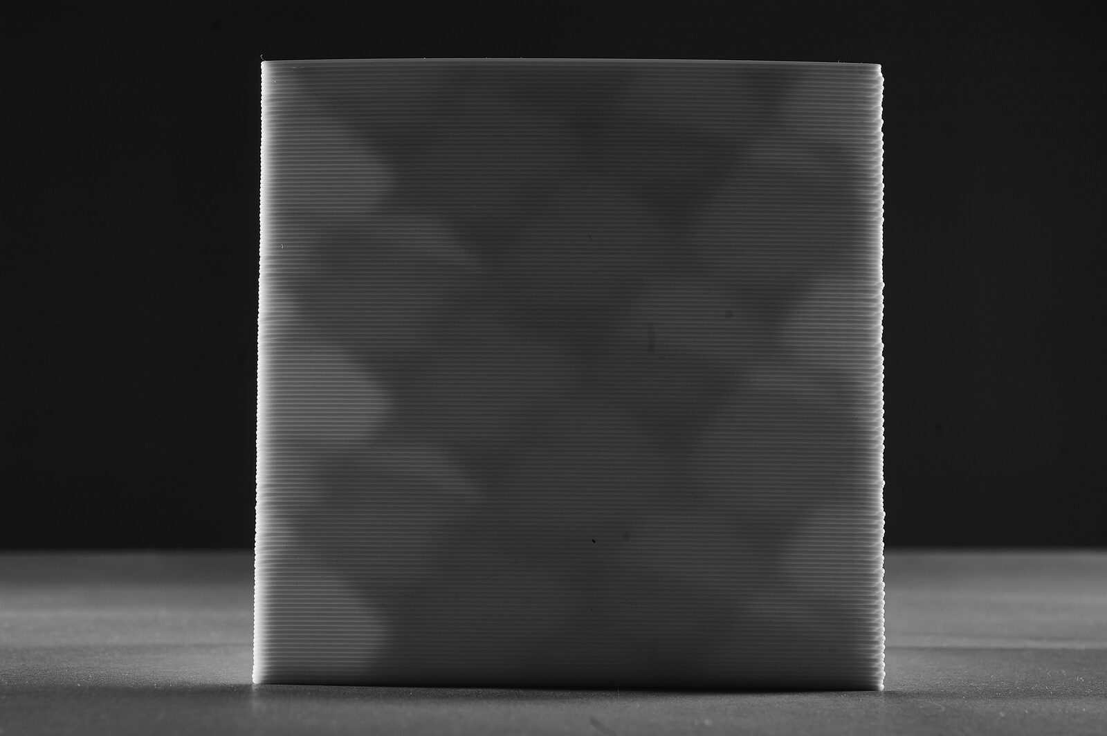 A printed cube lit from the side, a diamond lattice showing faintly through its wall and the top edge visibly curved
