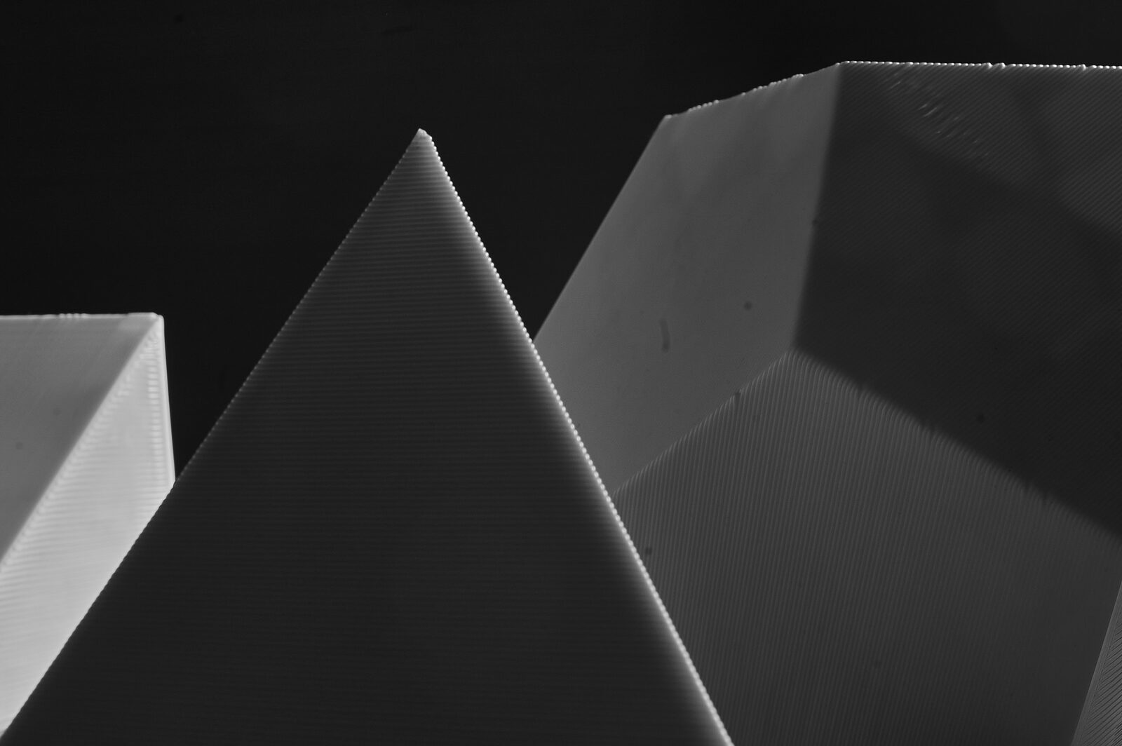 Close view of a tetrahedron apex against a dark ground, with an octahedron and a dodecahedron edge behind it, layer lines along every edge