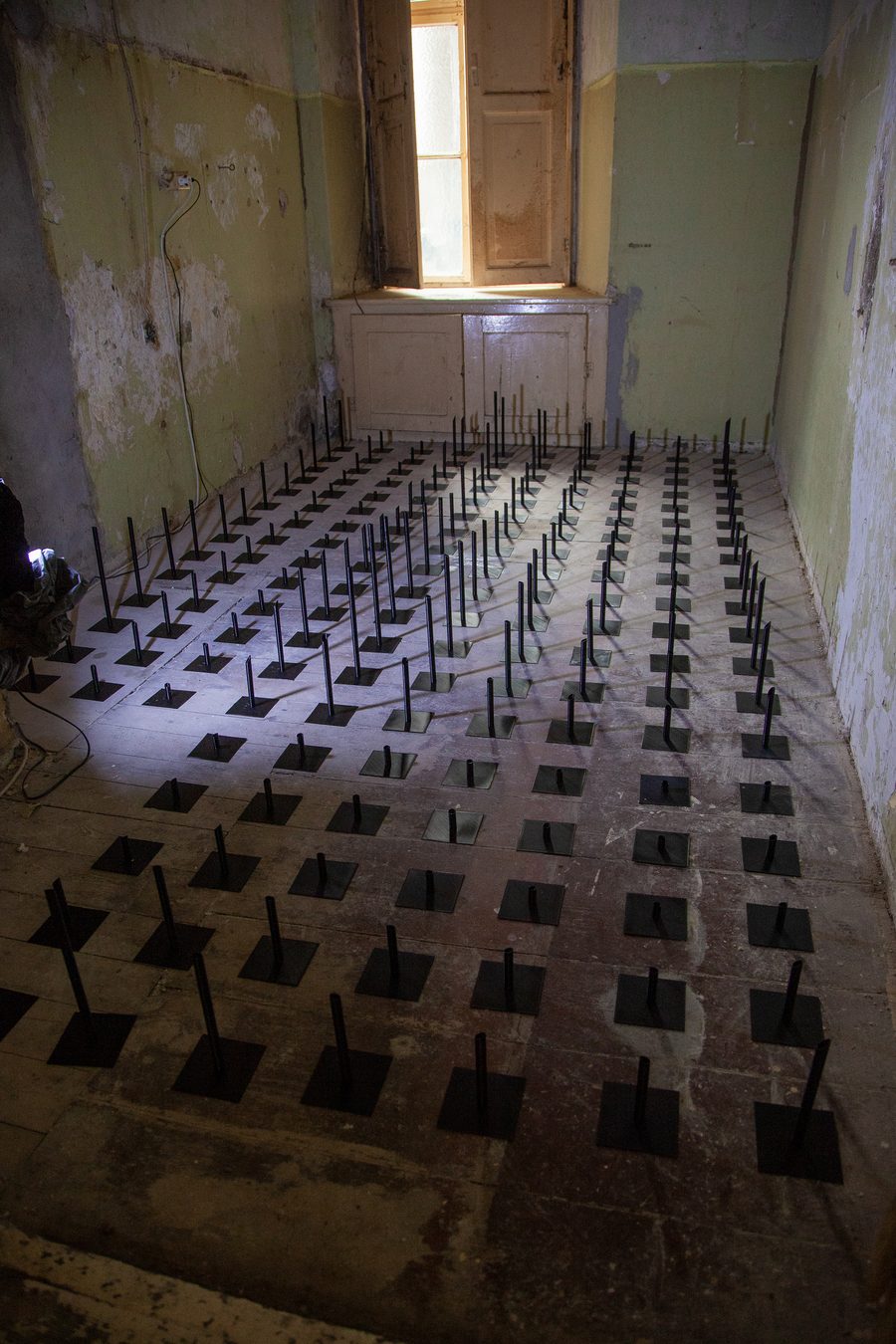 The field of tips installed across the floor of a bare room, lit by a tall window