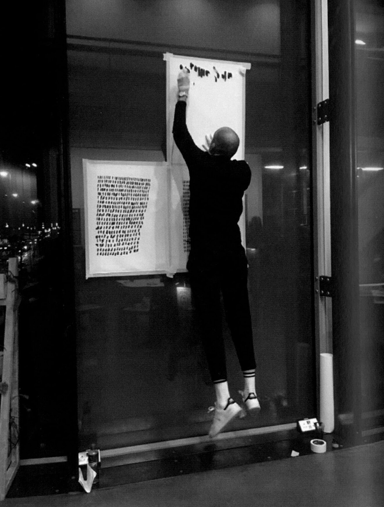 The artist at night in front of a glass wall, jumping to reach the top of a sheet mounted high