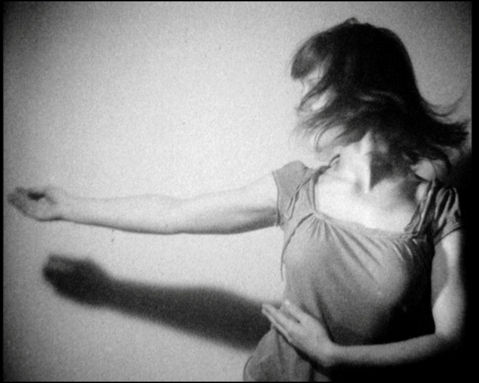 Both arms flung out to the left, hair thrown across the face, the wall bright behind