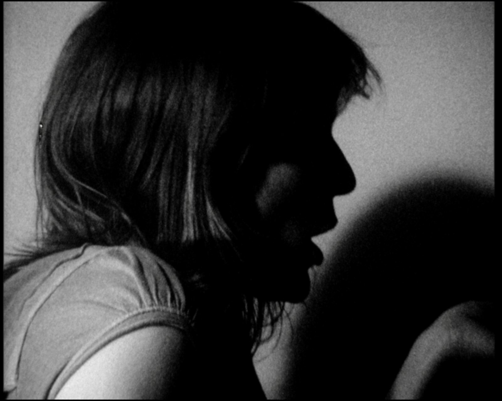 In profile facing right, mouth open, the wall bright behind her
