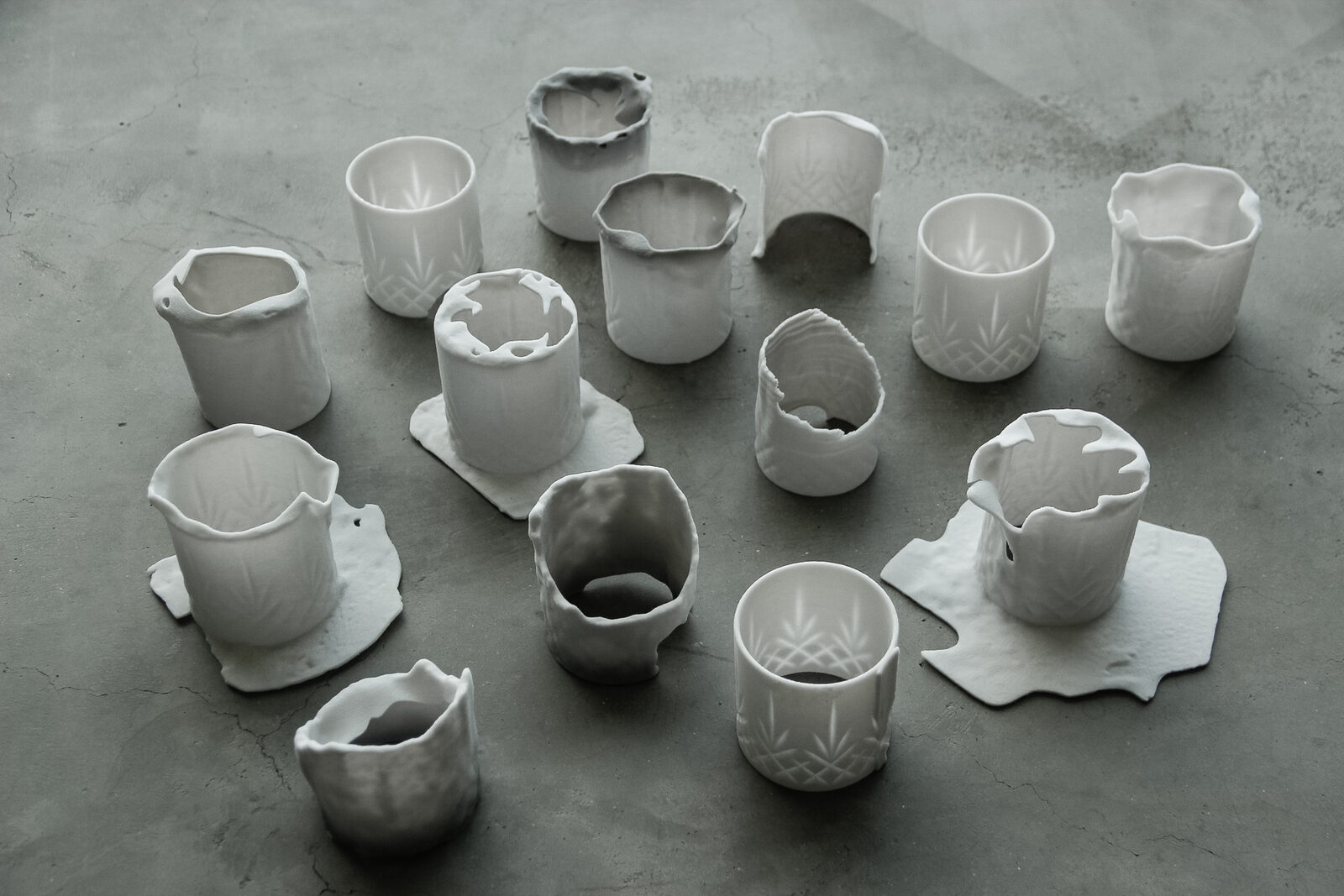 Many small white 3D-printed cups laid out on a concrete floor, each deformed differently