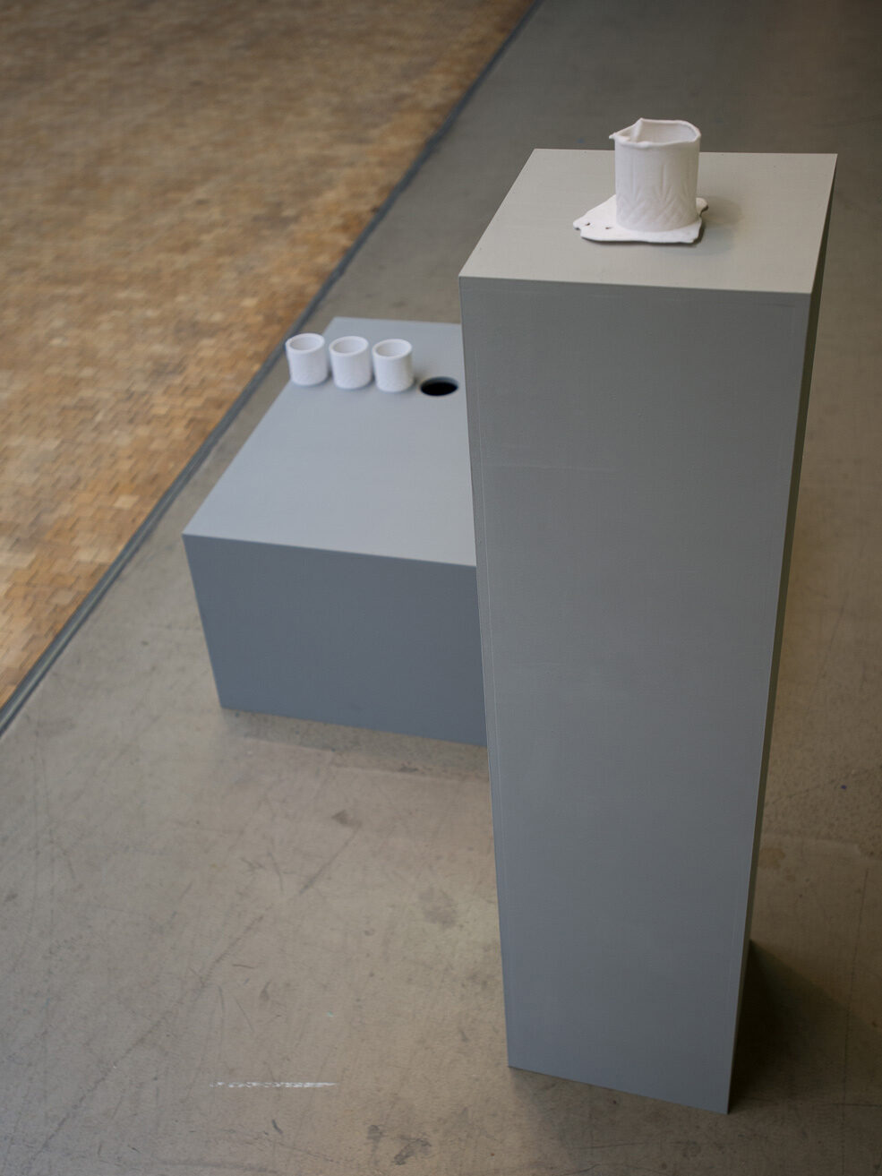 A tall plinth carrying one cup, with three smaller cups on a low block beside it