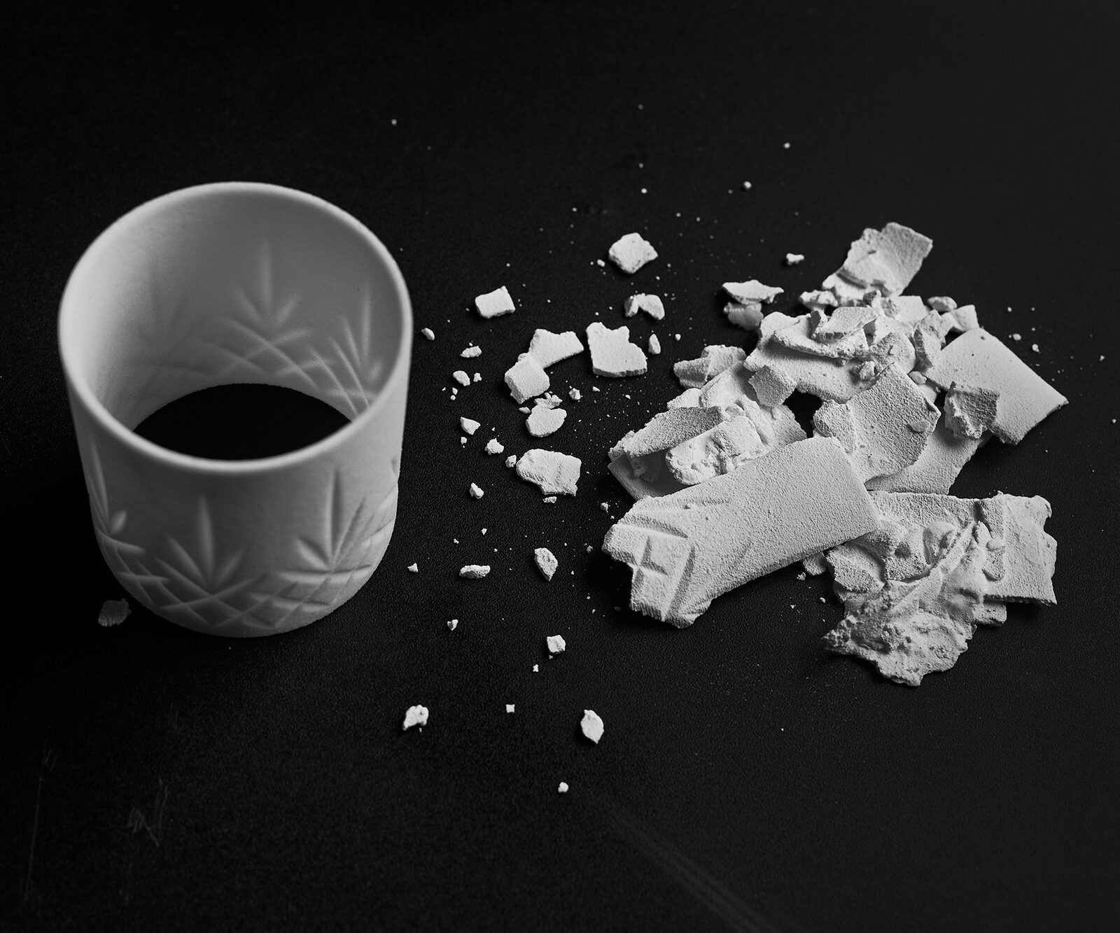 An intact white printed cup on a black ground with the shattered fragments of another beside it
