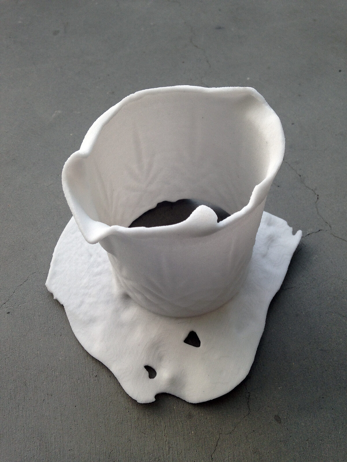 A single white cup standing on a crumpled printed sheet on concrete