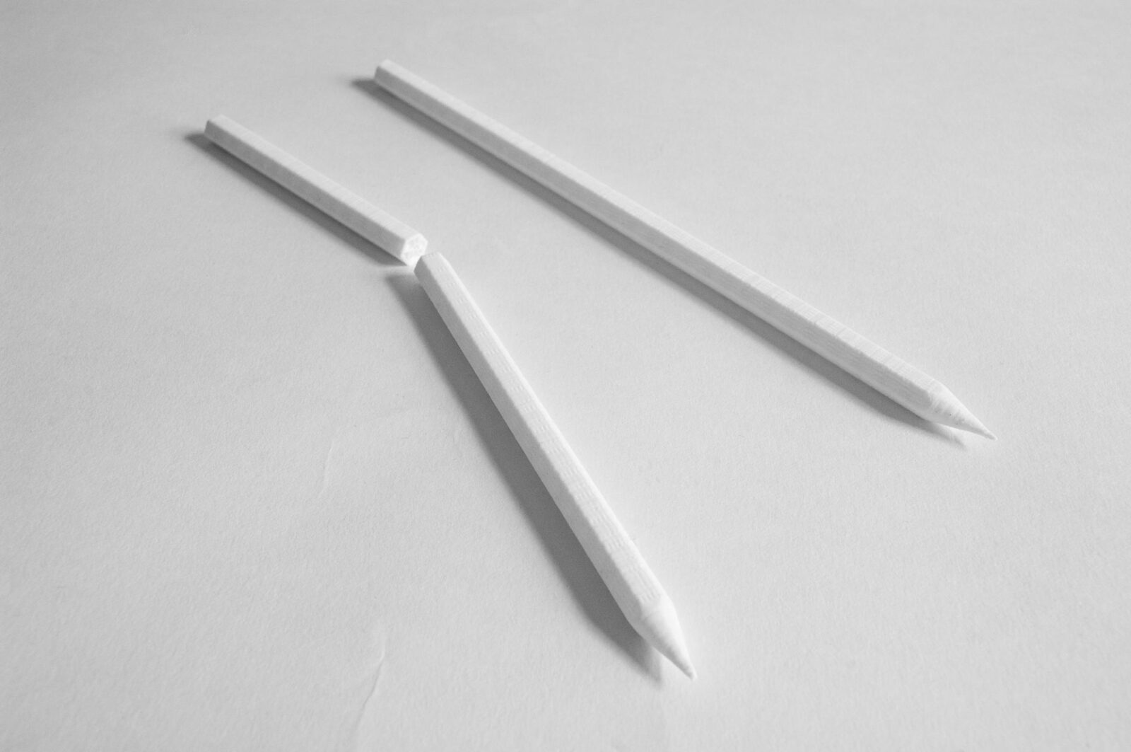 Two white 3D-printed pencils on a white surface, one snapped through the middle