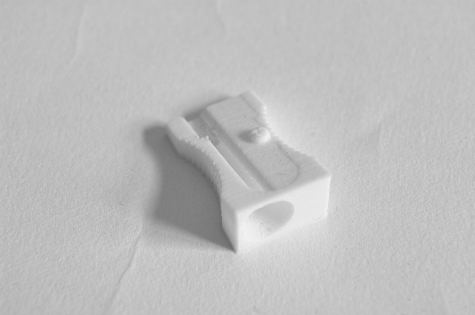 A white 3D-printed pencil sharpener, its layer lines visible along one flank