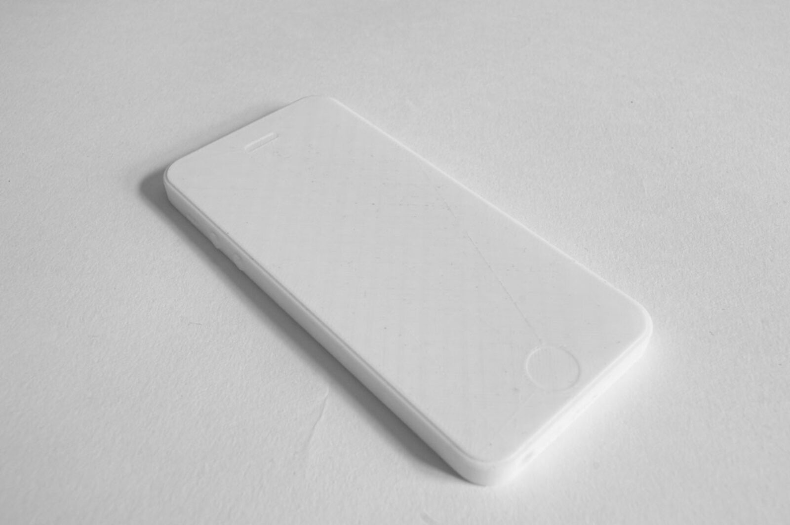 A white 3D-printed model of an iPhone lying face up on a white surface