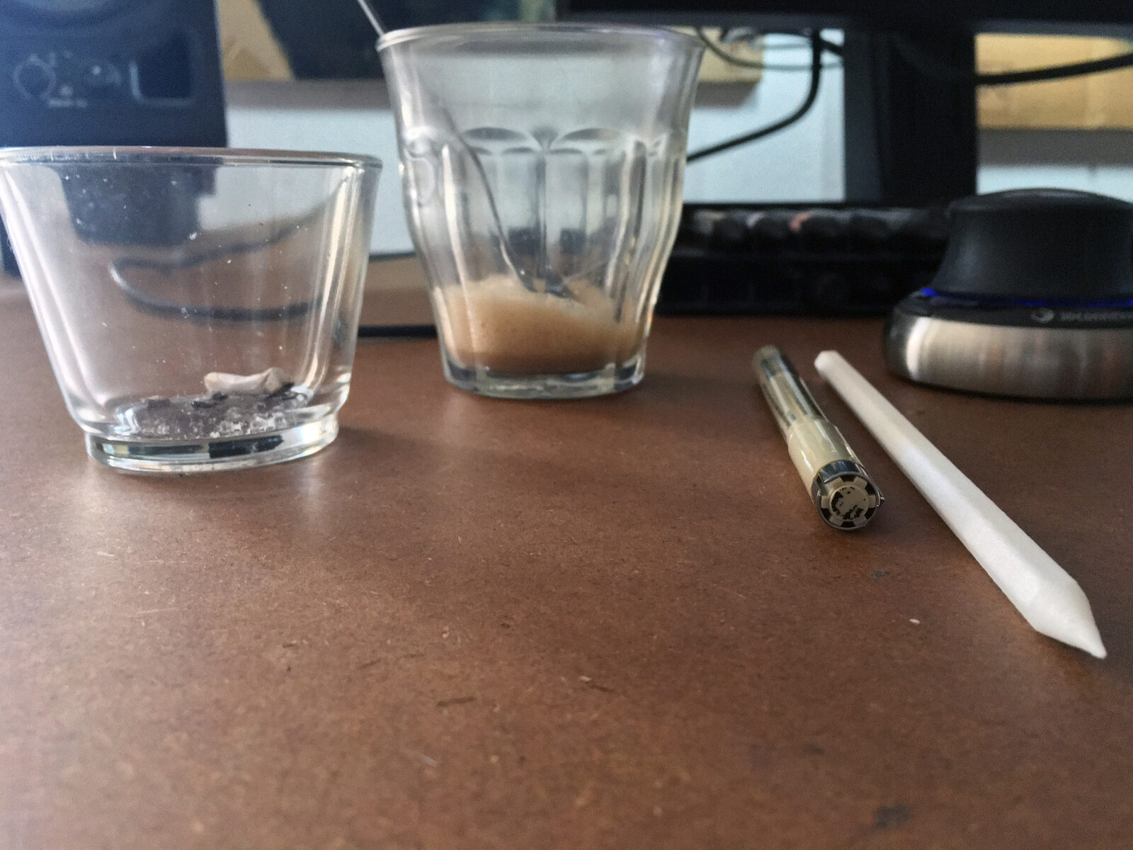 Two drinking glasses and a technical pen on a desk, with the white printed pencil beside them