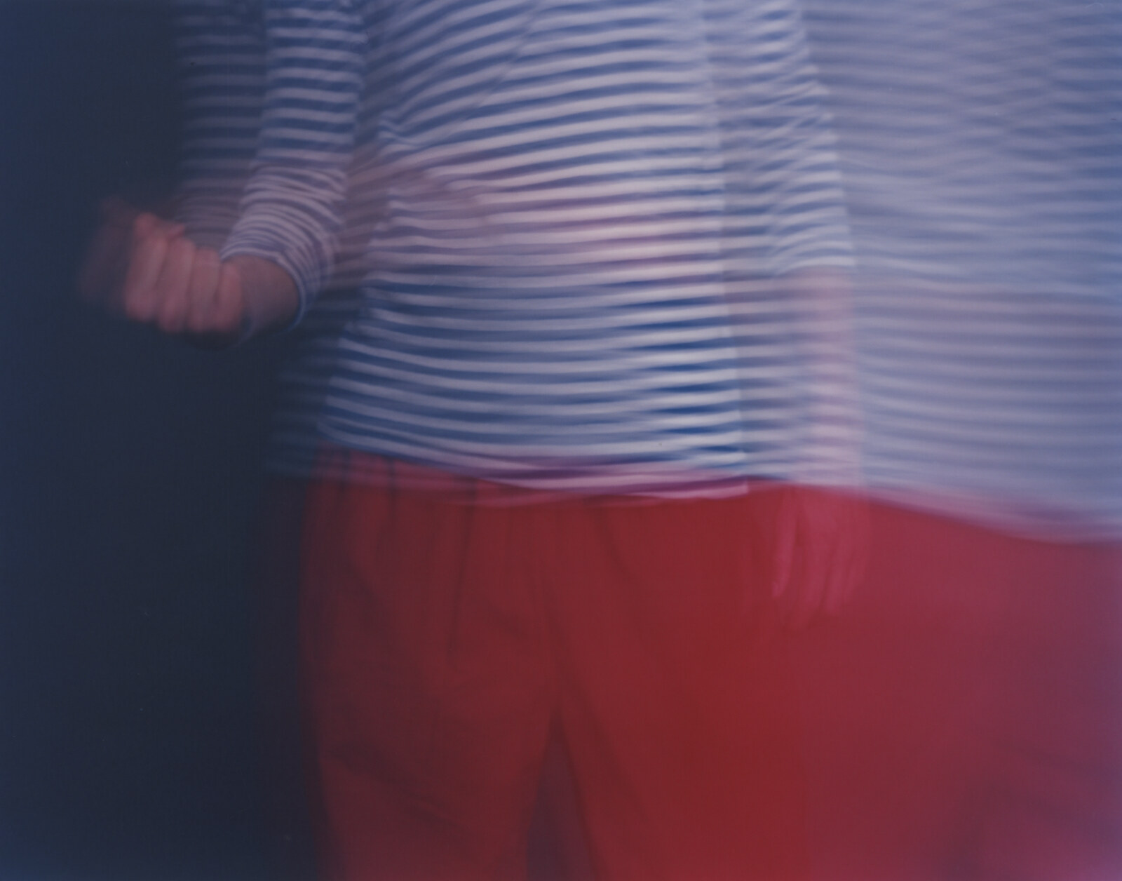A torso in a striped shirt smeared into horizontal waves, a fist held out at the left edge, red trousers filling the lower half against a dark blue ground