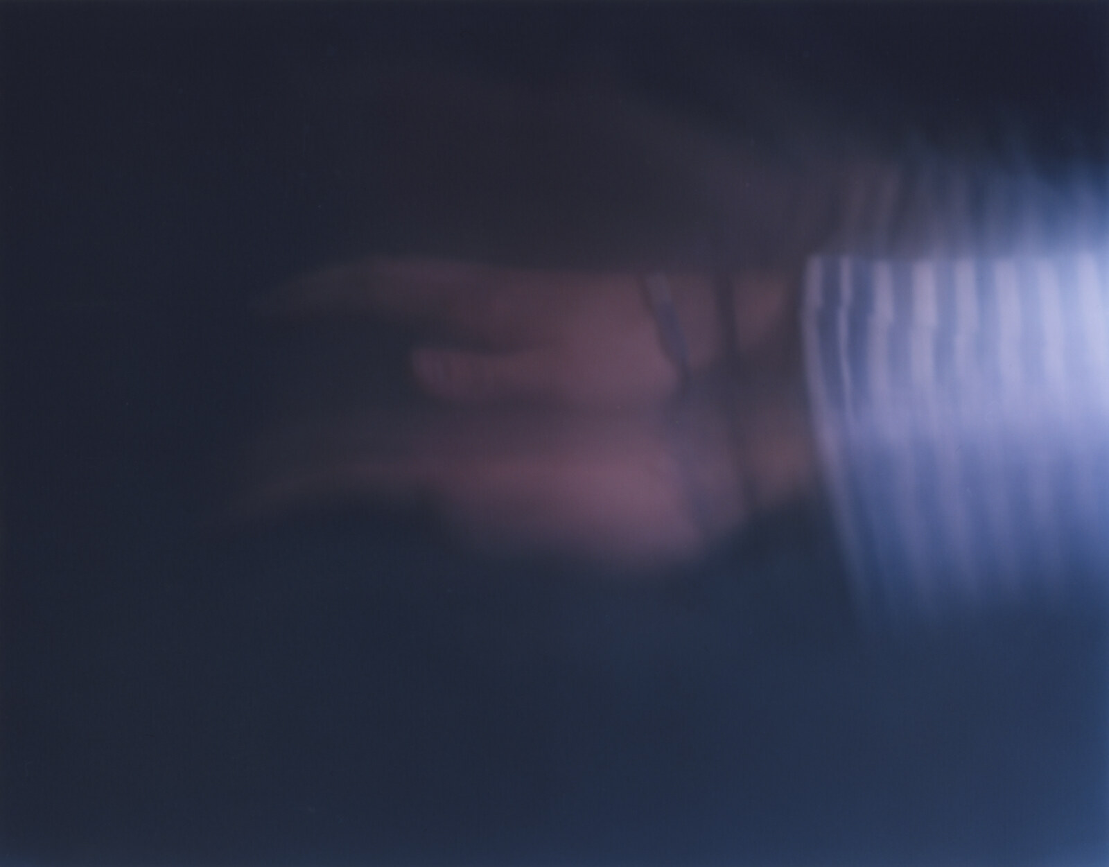 A pale arm sweeping across a near-black field, the striped sleeve resolving into hard bands at the right edge
