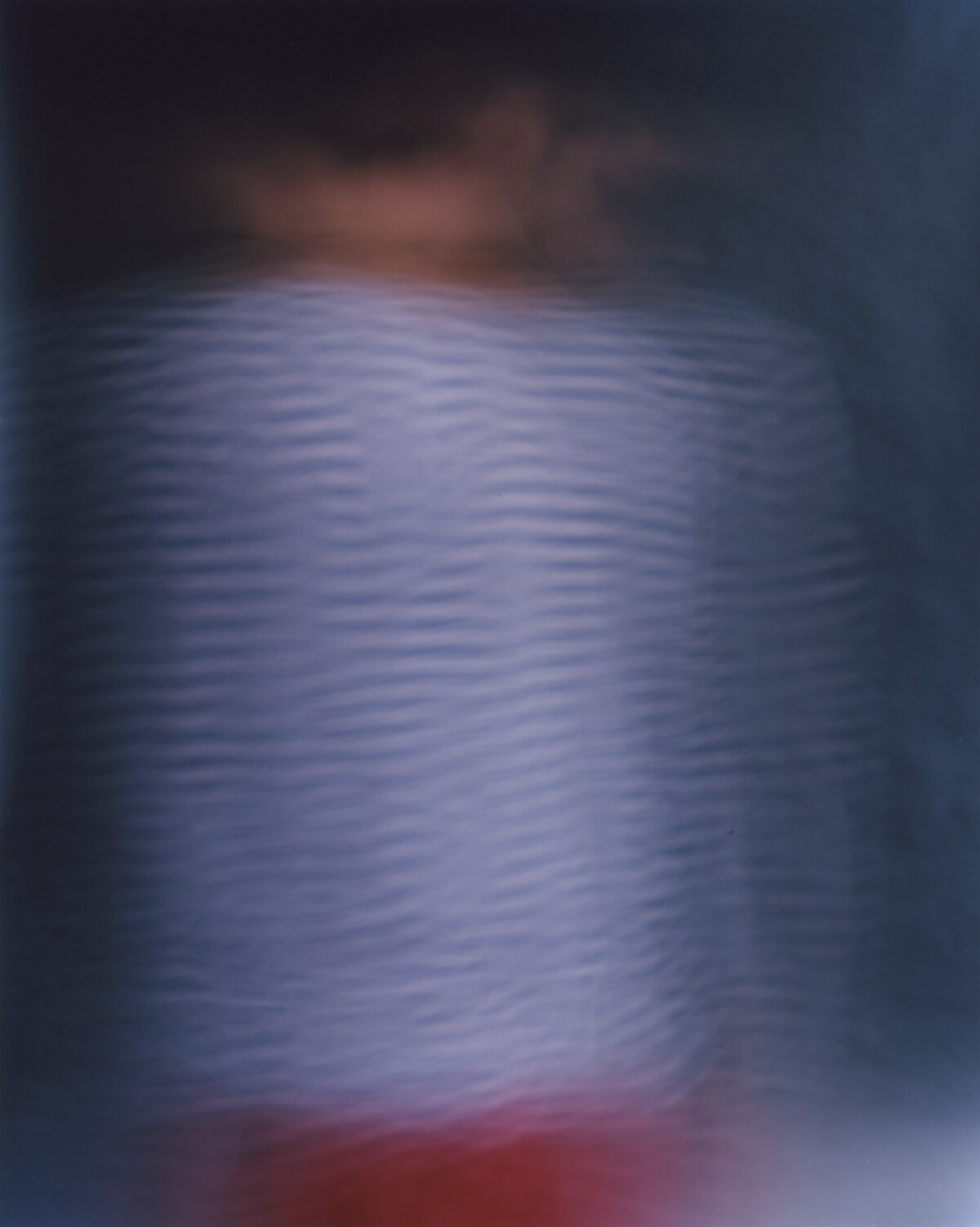 A striped torso held at the centre of the frame, the head above it dispersed into a dark smear, a red edge entering at the bottom