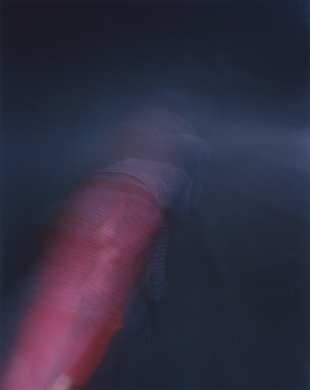 A red limb running diagonally down the frame, striped fabric breaking across the top, the rest sunk into dark blue