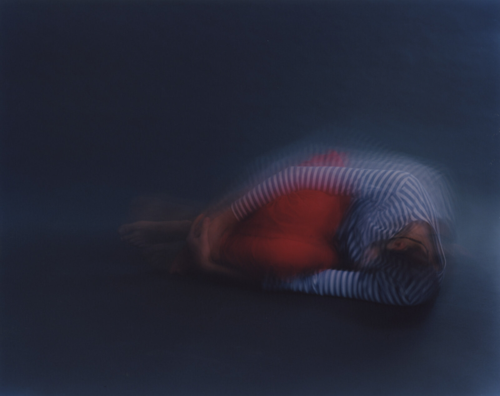The figure low and folded on the floor, the striped back arched, red showing beneath it, the ground a flat blue-grey