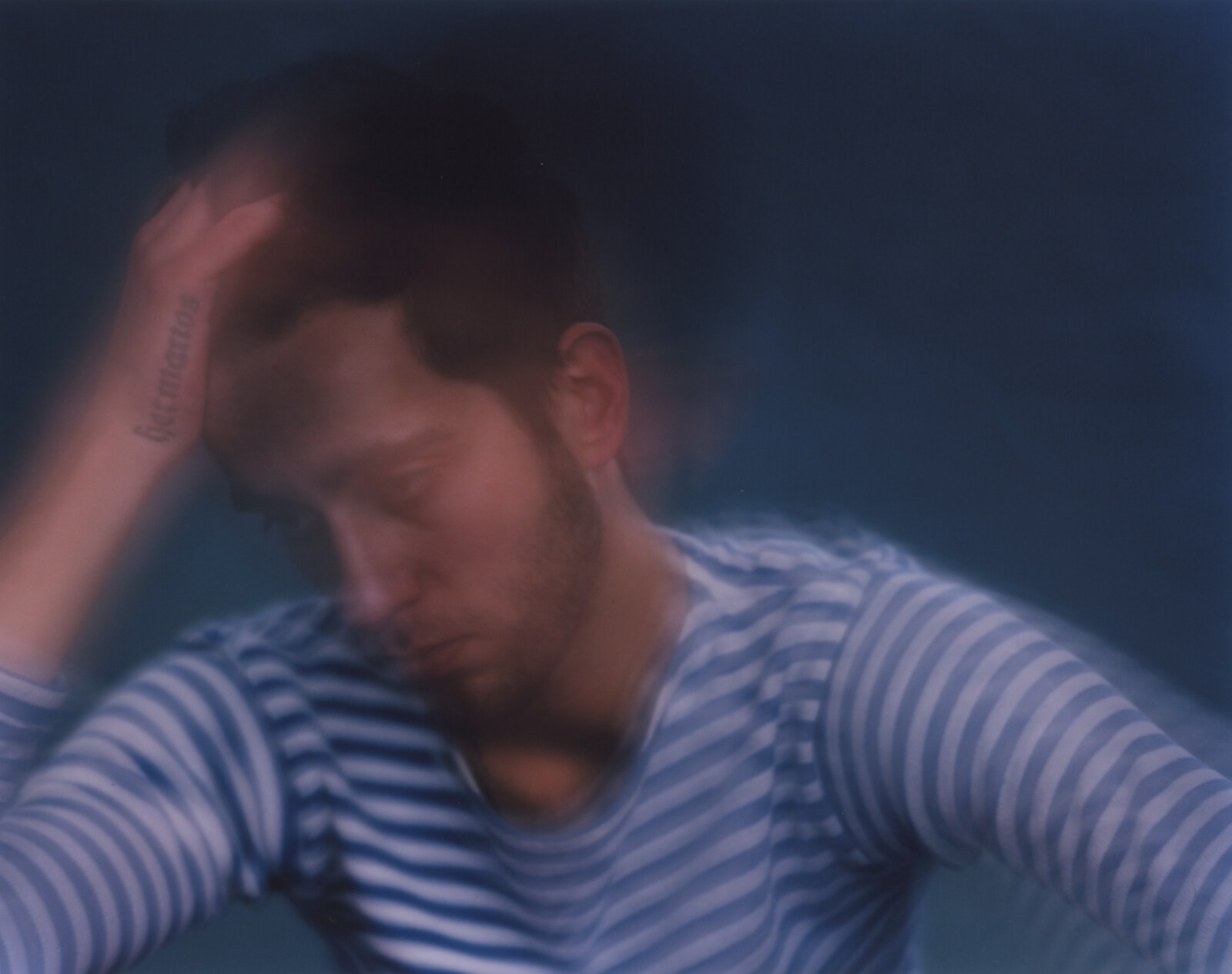 Head and shoulders resolving out of the blur, both hands raised into the hair, the striped shirt holding its bands across the lower frame