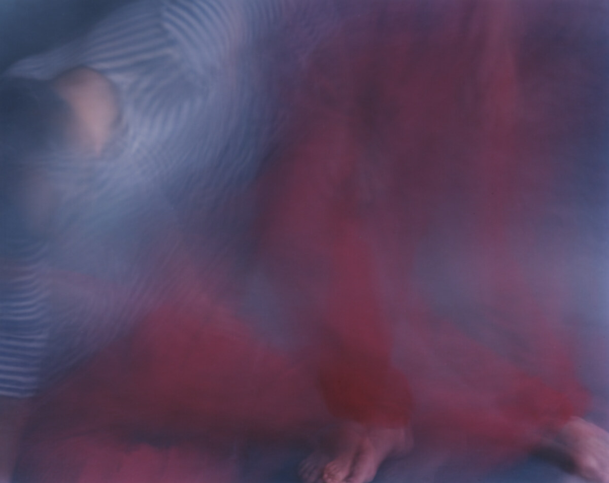 A thirty-second exposure of a figure on the floor: the red trousers spread into a mass of colour, bare feet resolving at the bottom edge