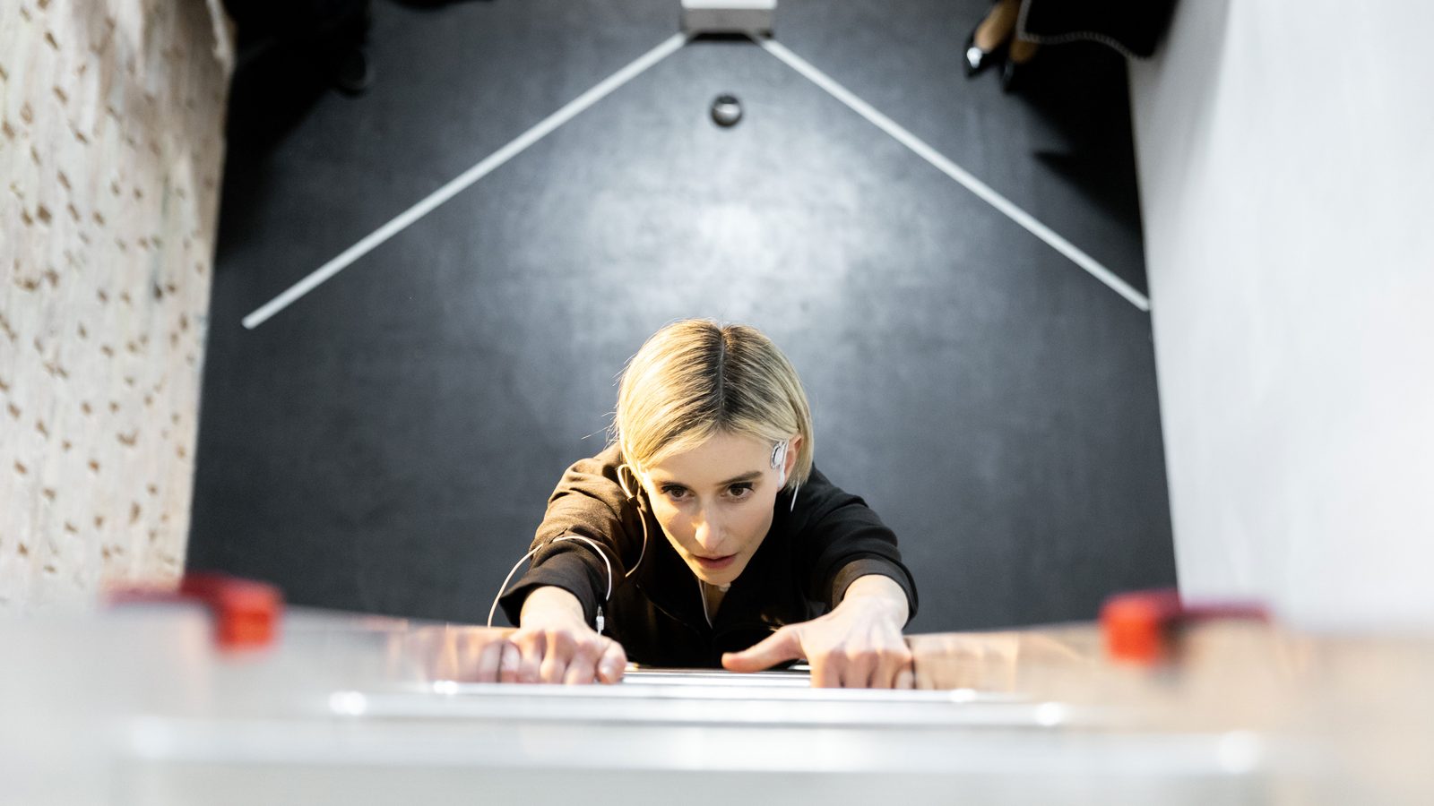 Seen from above through the opening under the roof: Katz climbing up towards the camera, her hands on the top rung, the gallery floor two storeys below