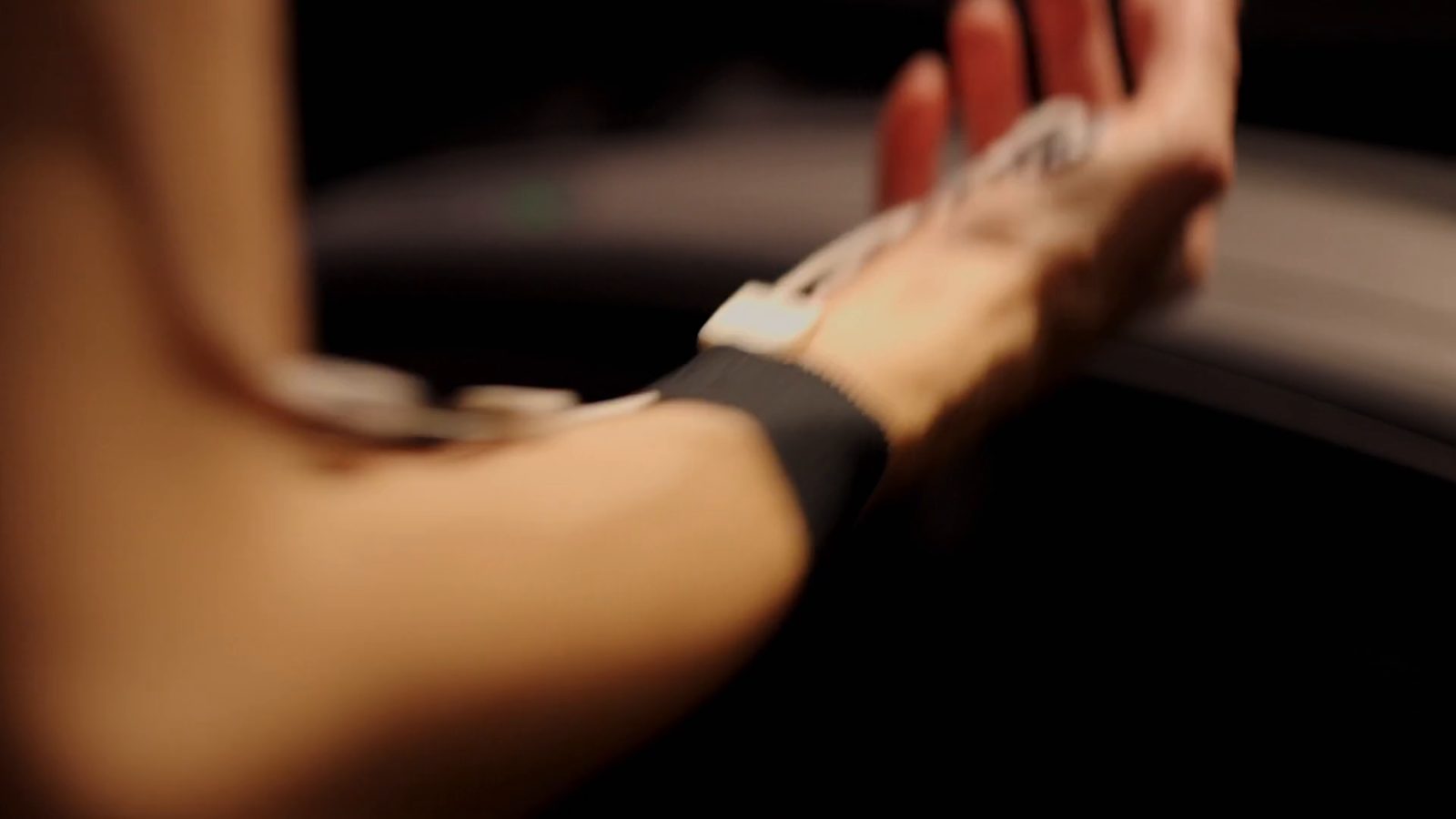 Katz’s forearm swinging past the treadmill rail, a sensor pad and its cable on the wrist above a black strap, the open hand blurred