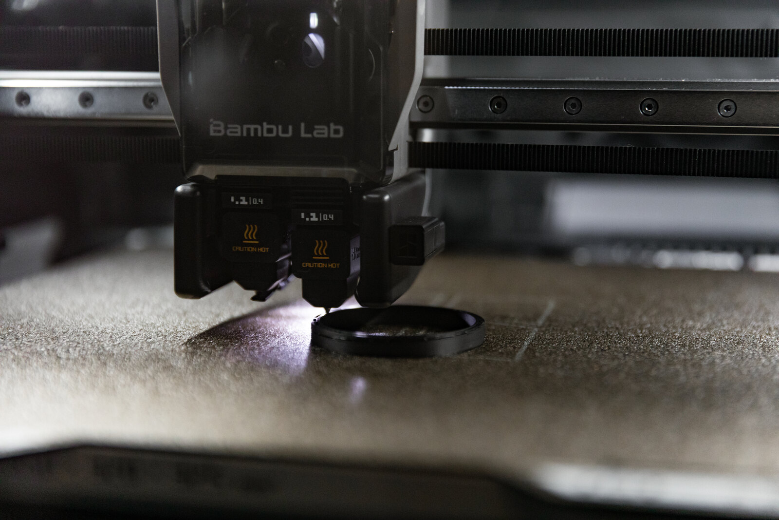 Close view of a print head laying a layer onto the rim of a black cylinder, the printer's gantry filling the frame behind it