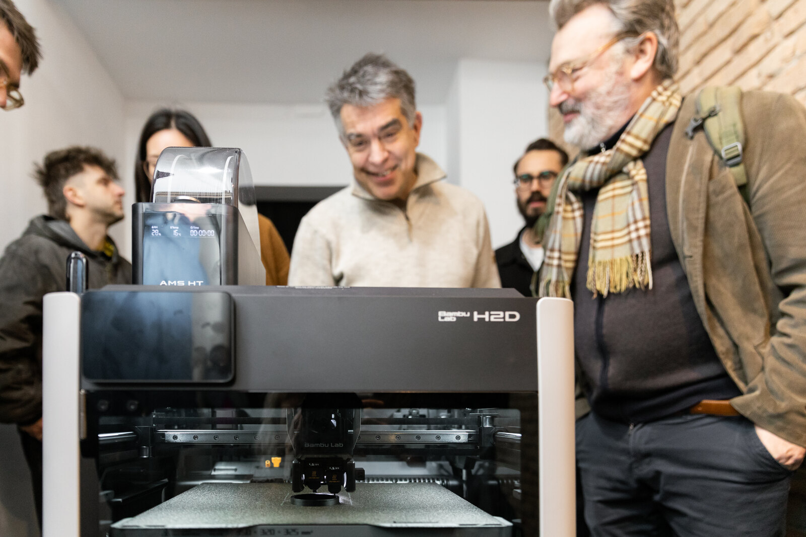 Visitors leaning over the open printer as it works, the machine at waist height between them