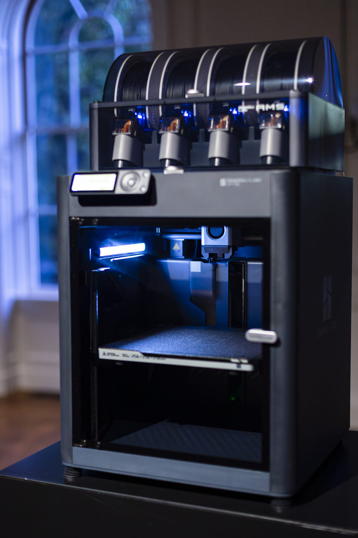 One printer on its stand, four filament feeds ranked across the top, the chamber lit from within