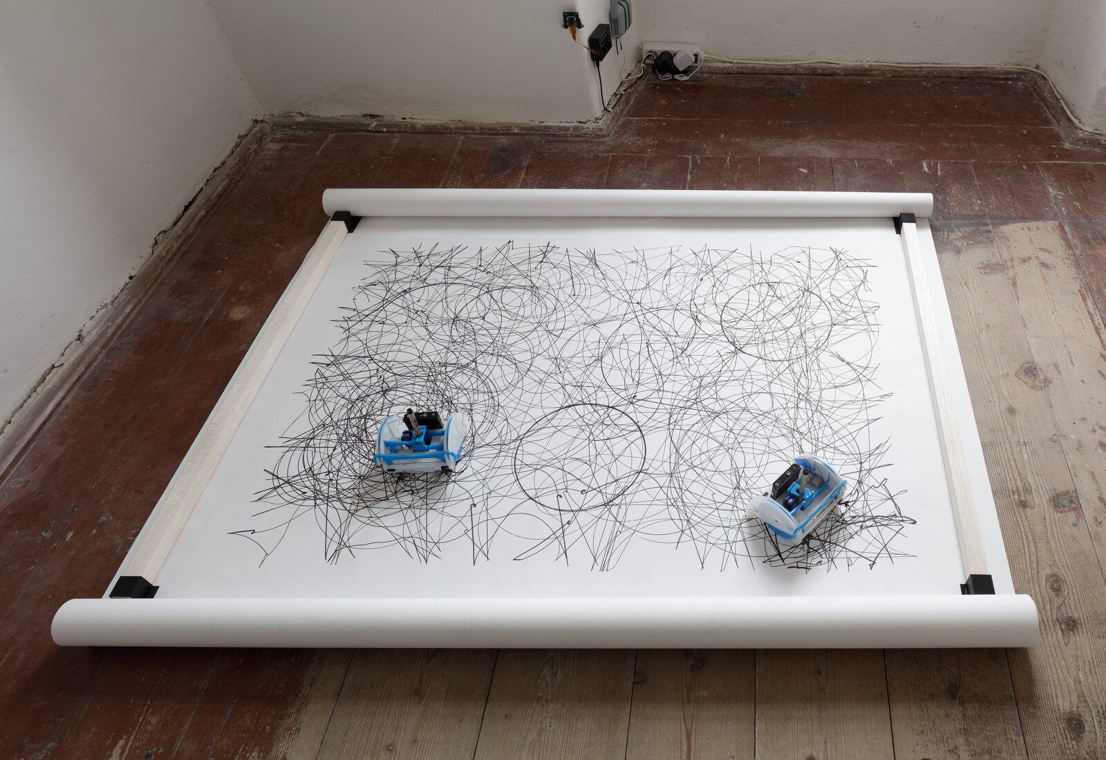 The paper band seen from above, dense with overlapping ink circles, a drawing robot resting at either end and one clean unmarked circle between them