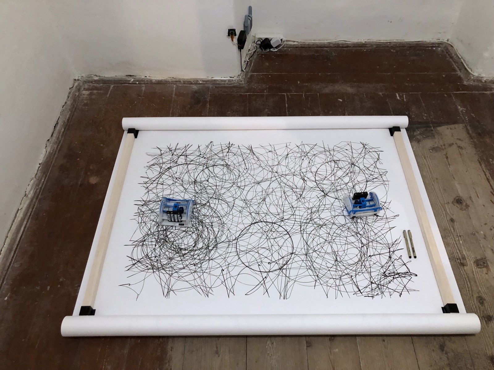 A later band, densely worked across its whole width in thin overlapping line, both robots resting in it and two spare brush pens lying on the paper at the right edge
