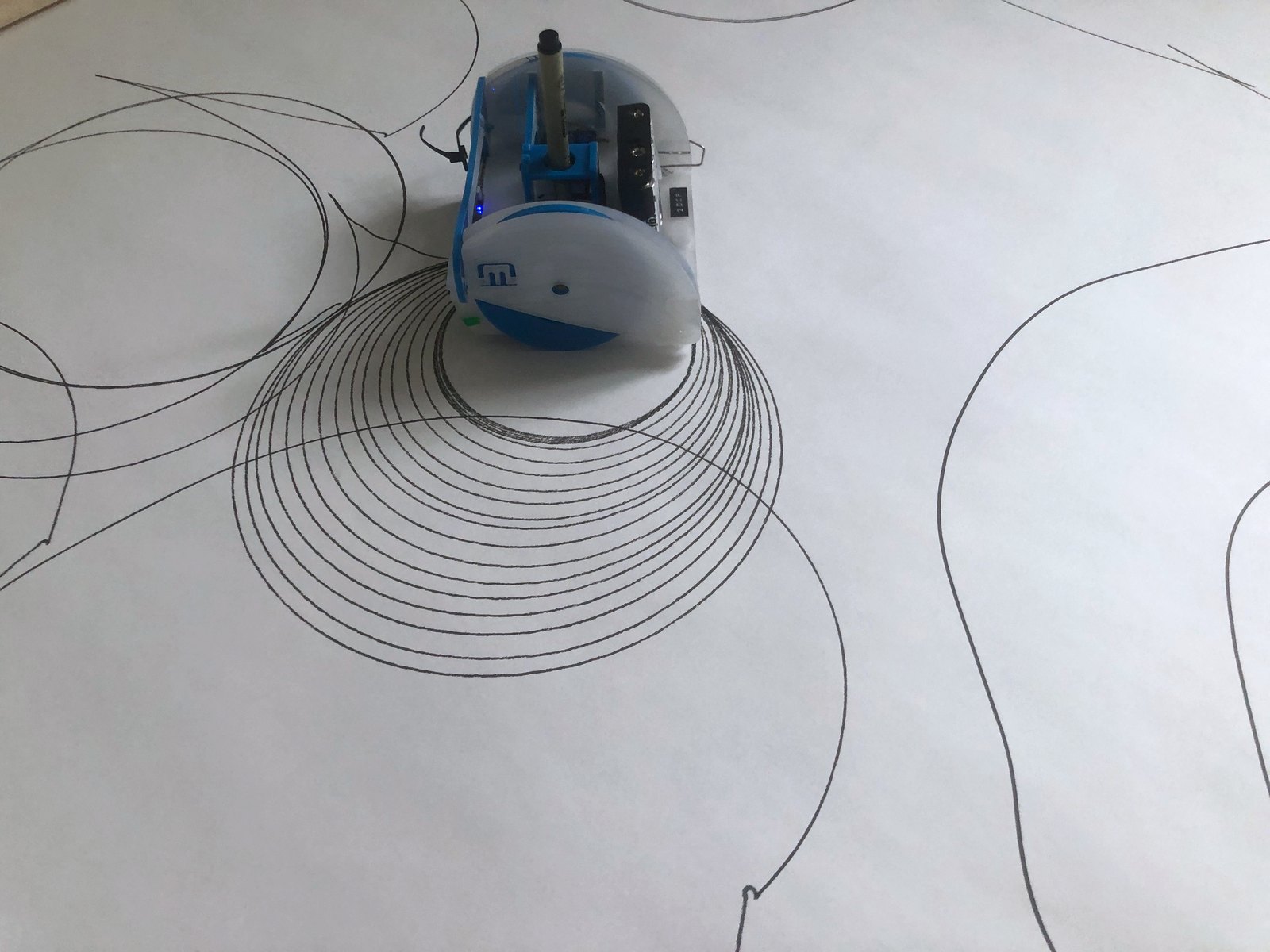 One robot seen from behind, resting at the end of a tight spiral of concentric rings it has just drawn
