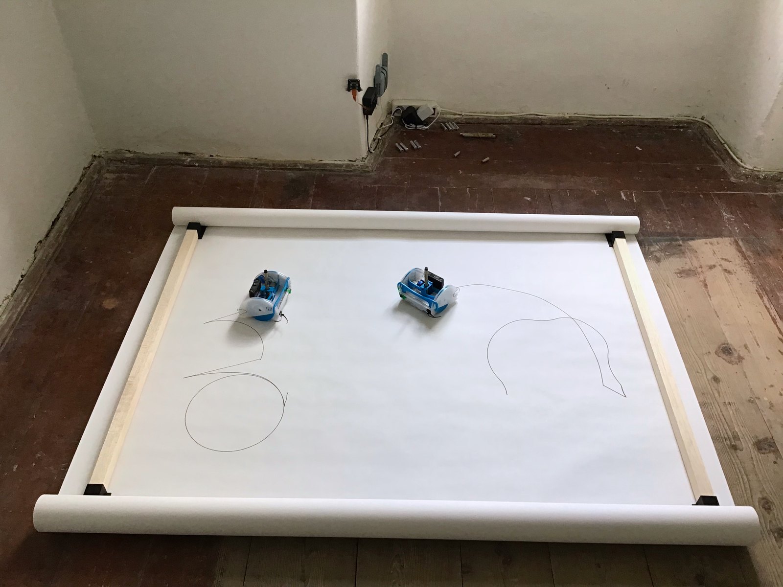 The room on the last day: a fresh band clamped between the battens, both robots near its centre, one circle and a single curved line drawn so far