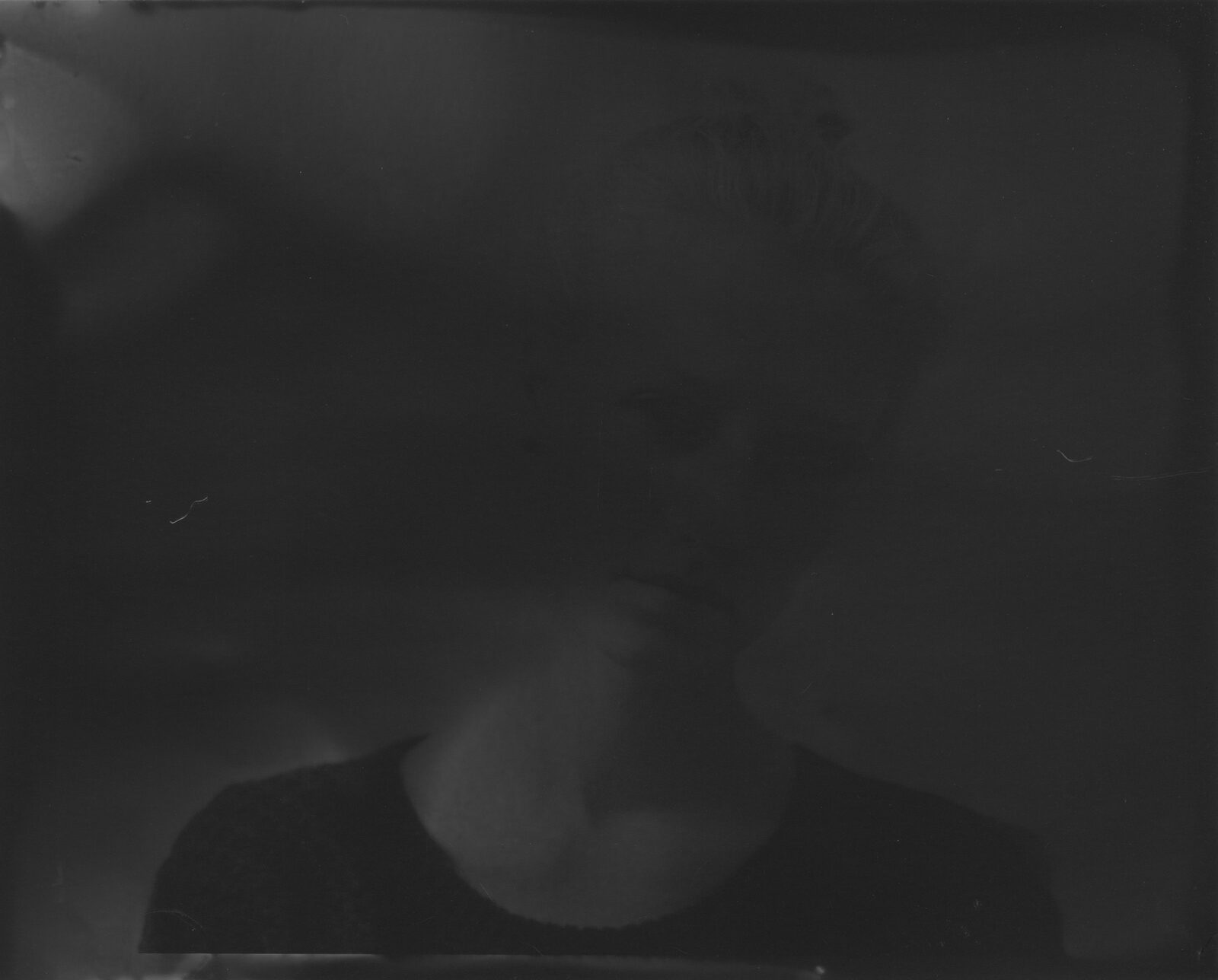 A very dark black-and-white print in which a face is barely discernible behind the darkness