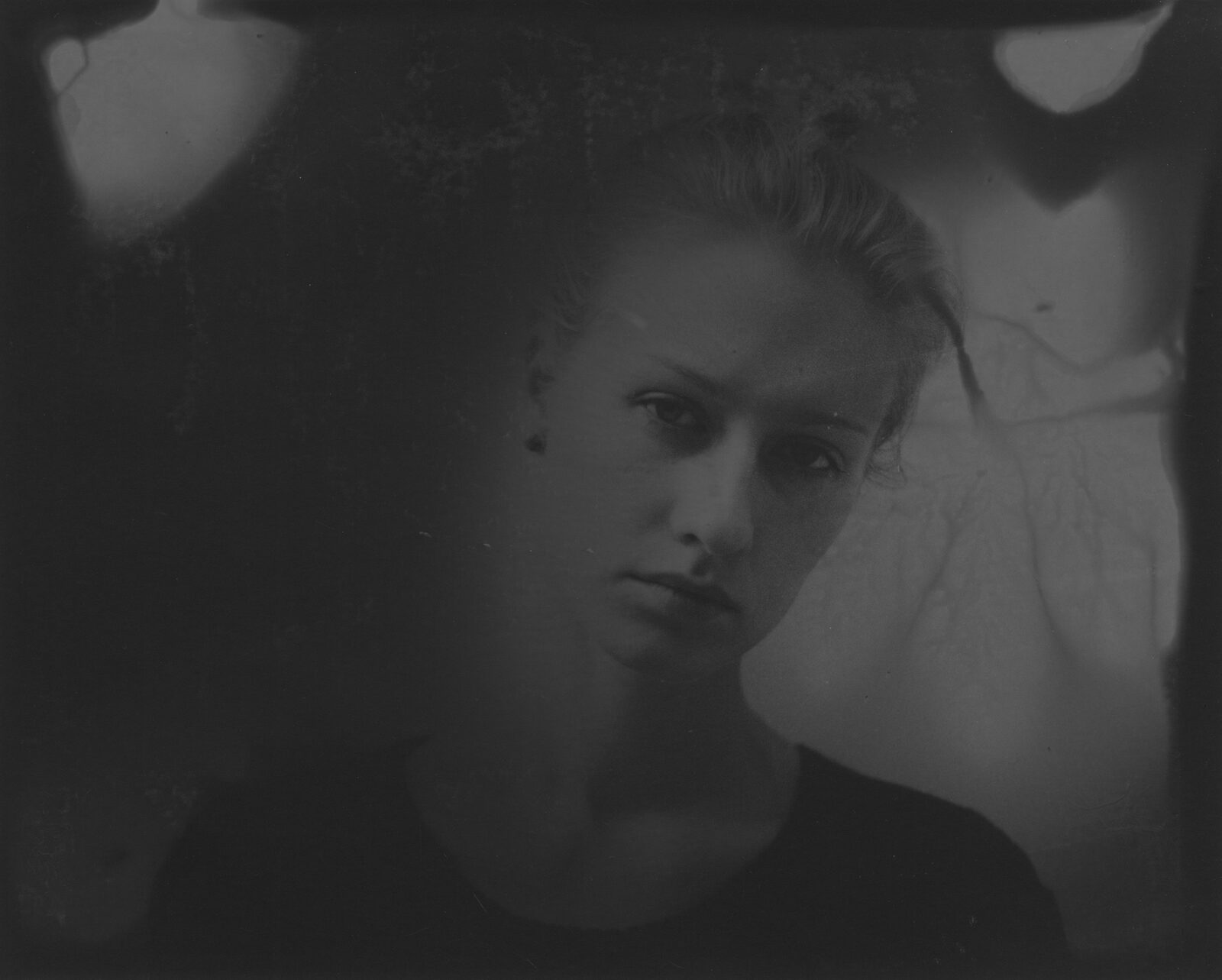 A very dark black-and-white analogue print in which a face surfaces from the darkness to a different degree
