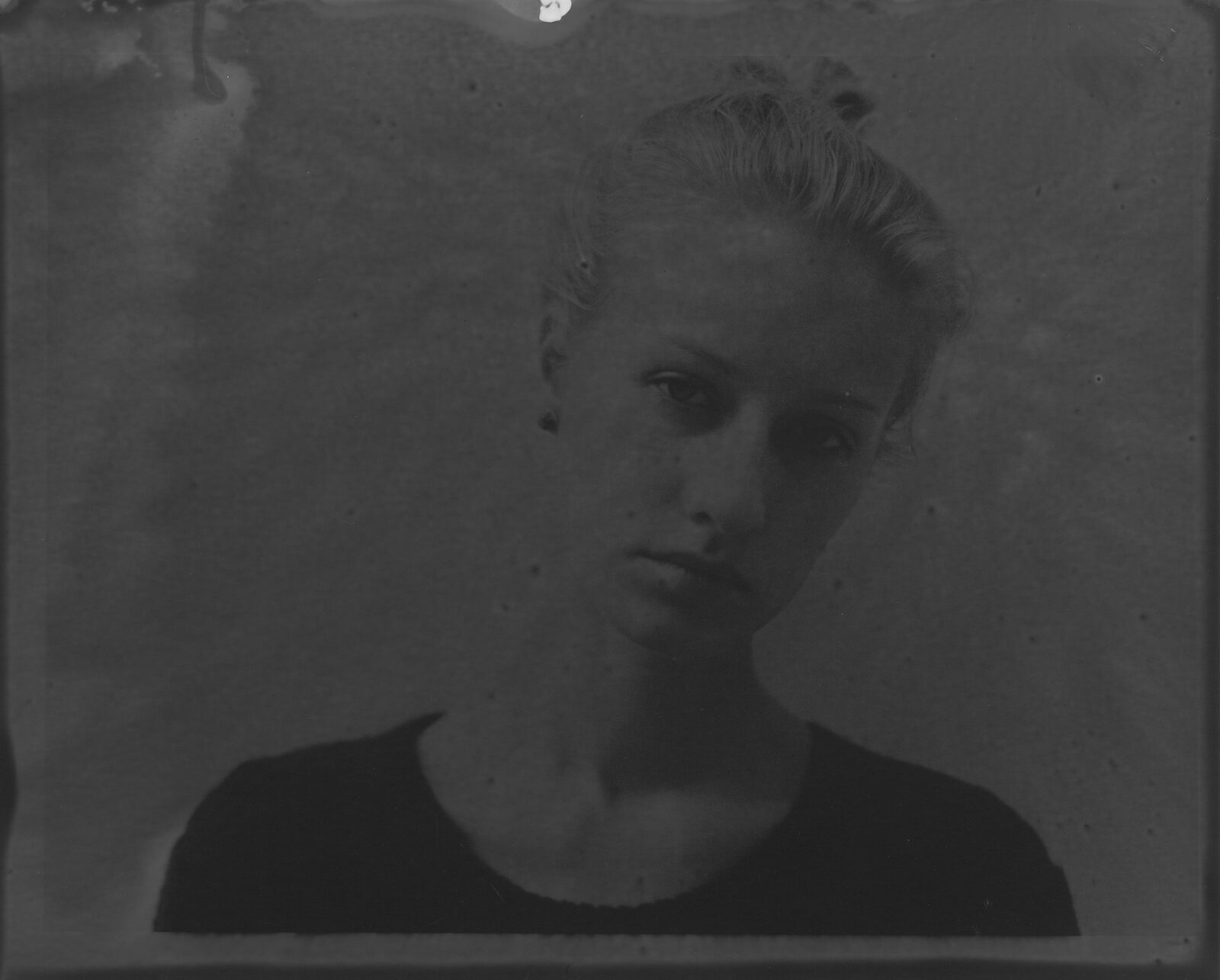 A very dark black-and-white analogue print in which a face surfaces from the darkness to a different degree