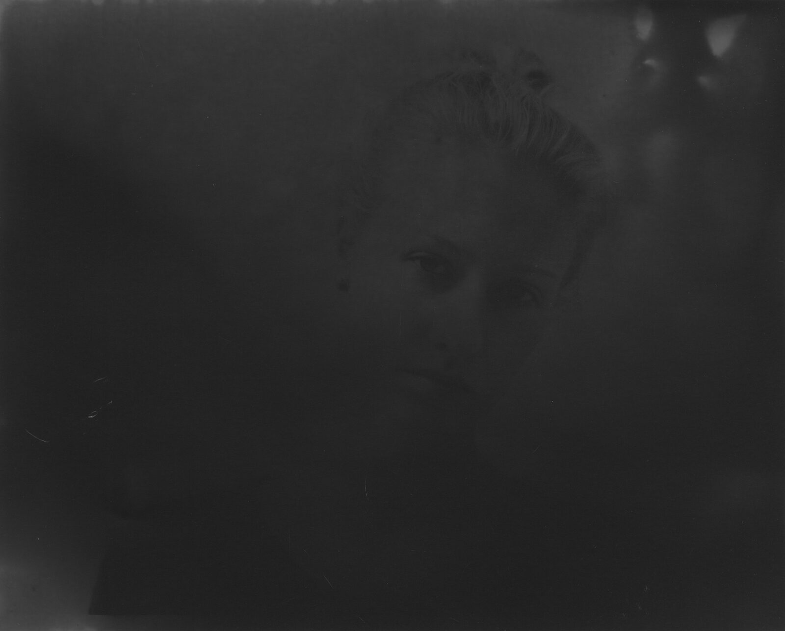 A very dark black-and-white analogue print in which a face surfaces from the darkness to a different degree
