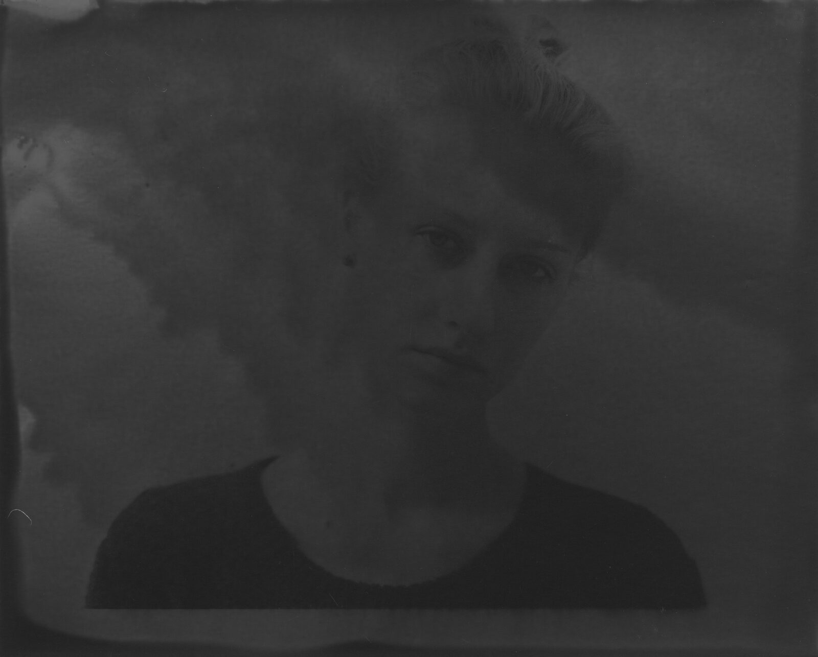 A very dark black-and-white analogue print in which a face surfaces from the darkness to a different degree