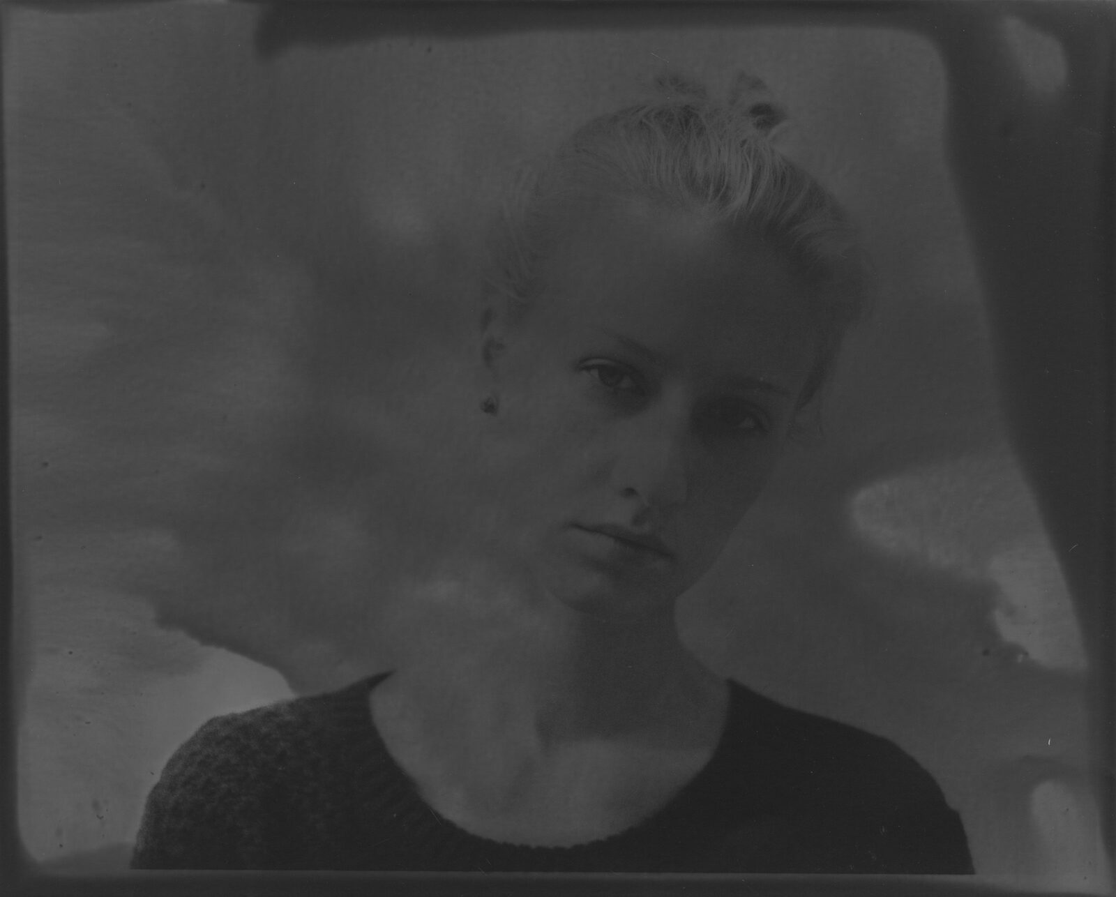 A very dark black-and-white analogue print in which a face surfaces from the darkness to a different degree