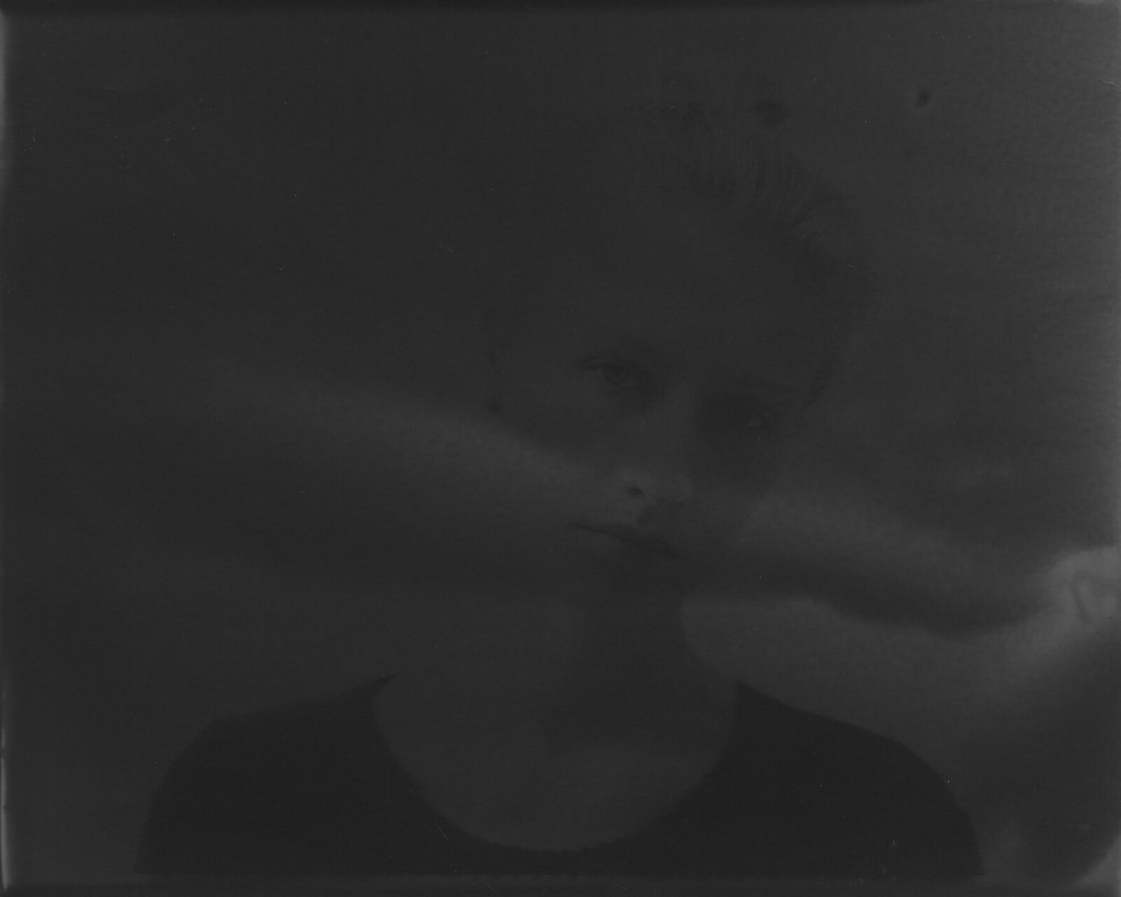 A very dark black-and-white analogue print in which a face surfaces from the darkness to a different degree