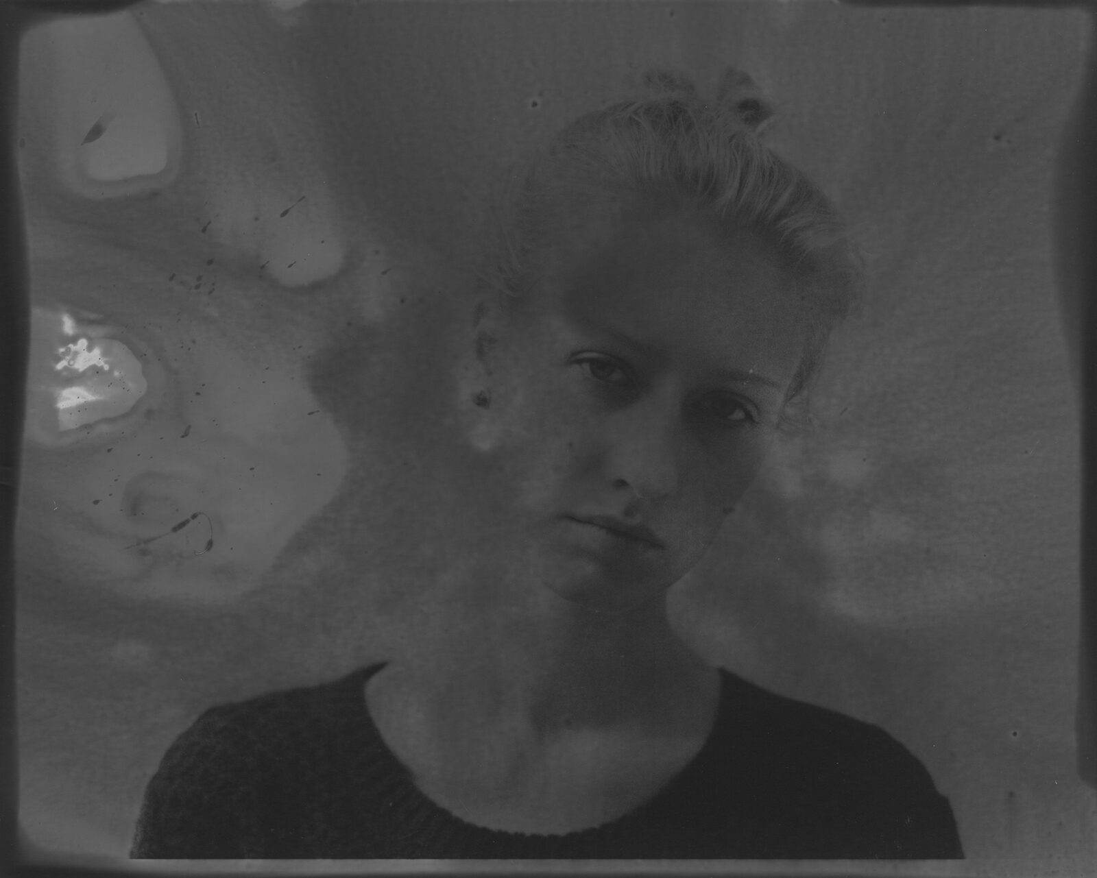 A very dark black-and-white analogue print in which a face surfaces from the darkness to a different degree