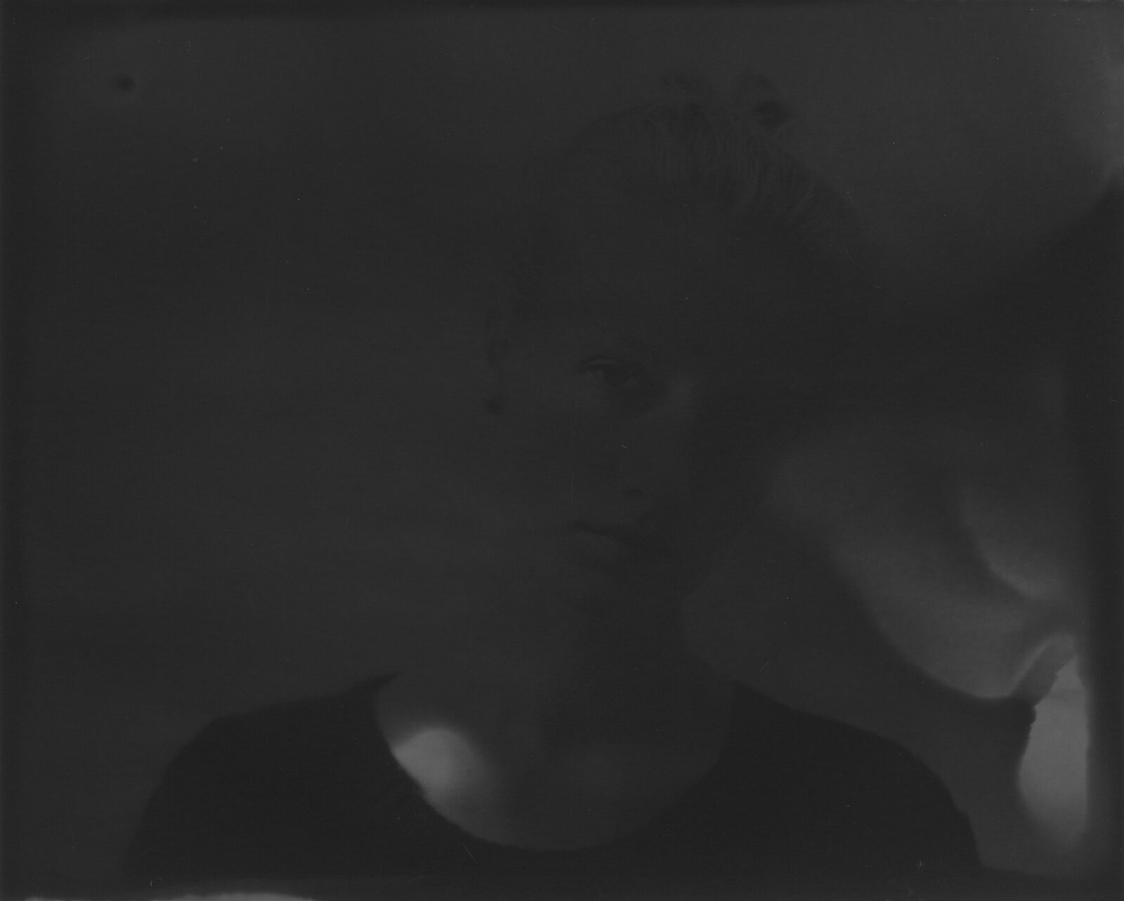 A very dark black-and-white analogue print in which a face surfaces from the darkness to a different degree