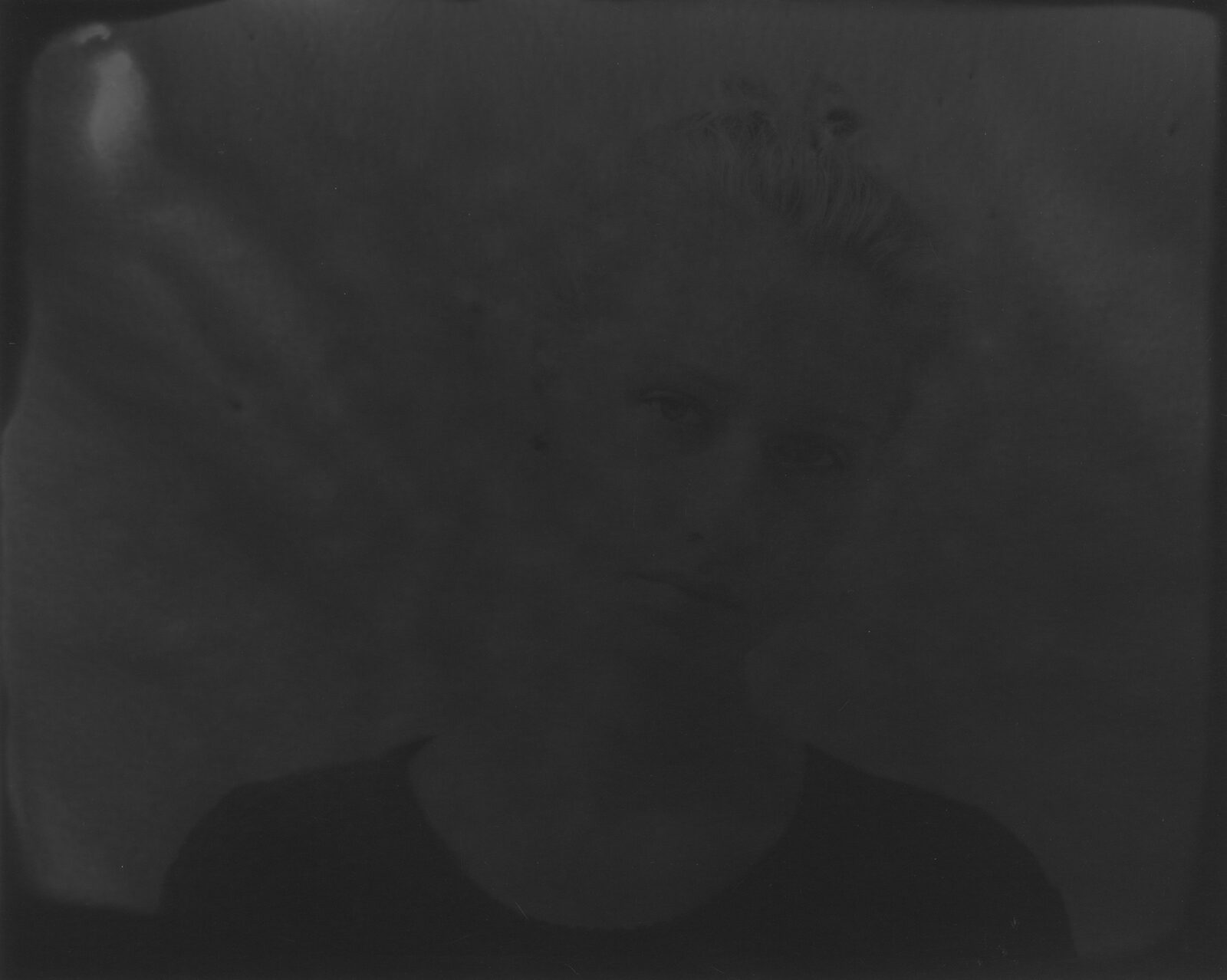 A very dark black-and-white analogue print in which a face surfaces from the darkness to a different degree