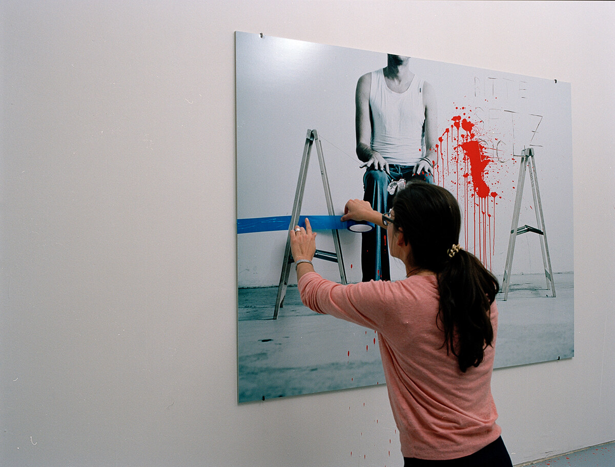 A woman reaching across the photograph, laying a blue line over the print