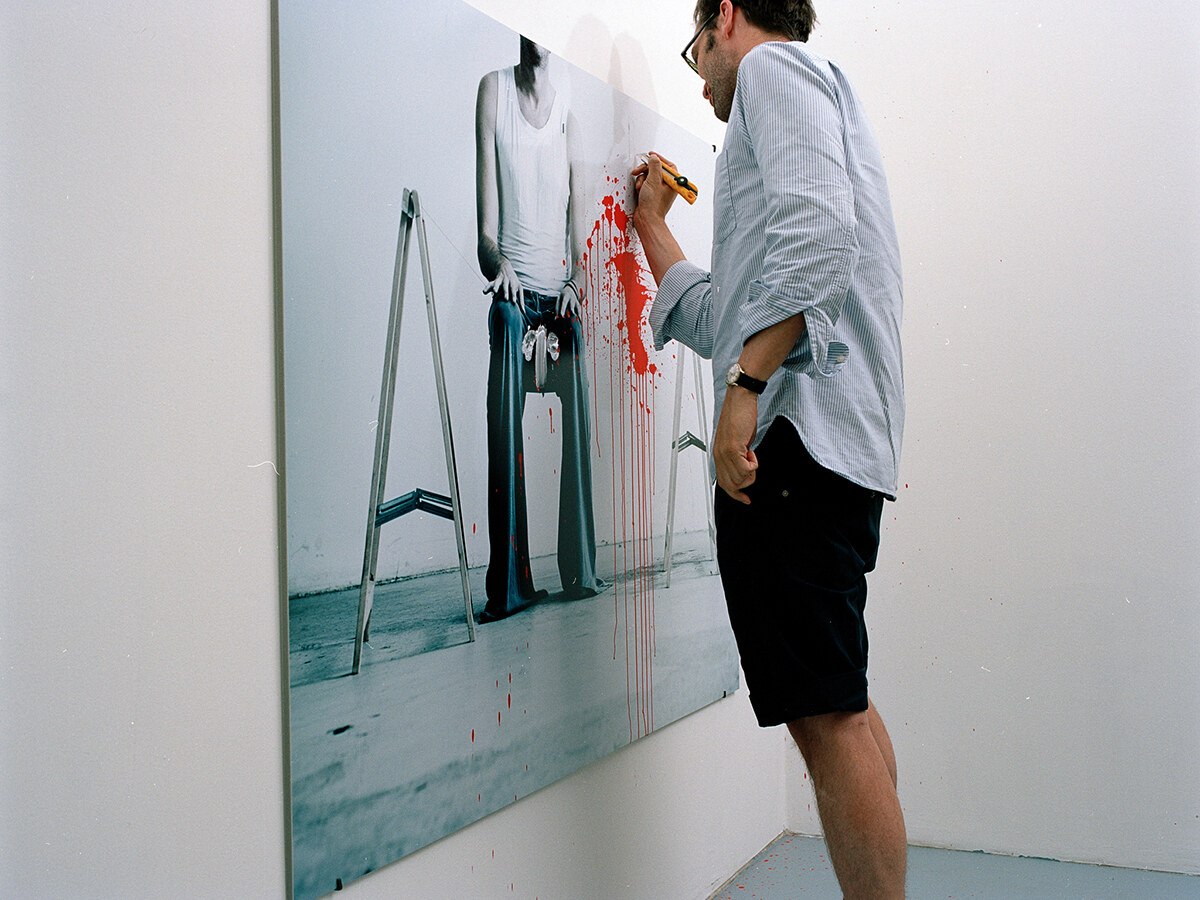 A man writing at the top of the photograph, the red splash and drips already present below his hand