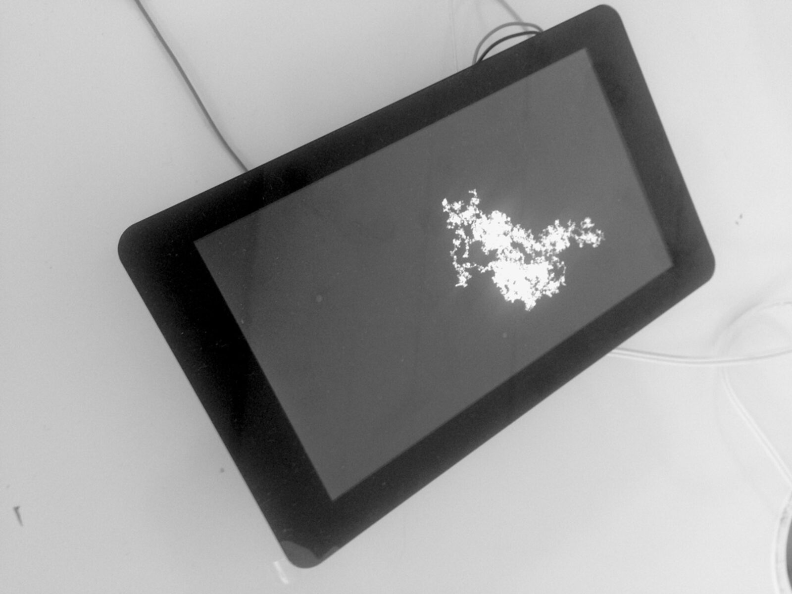 A screen lying on a white surface showing a white random-walk trace on black
